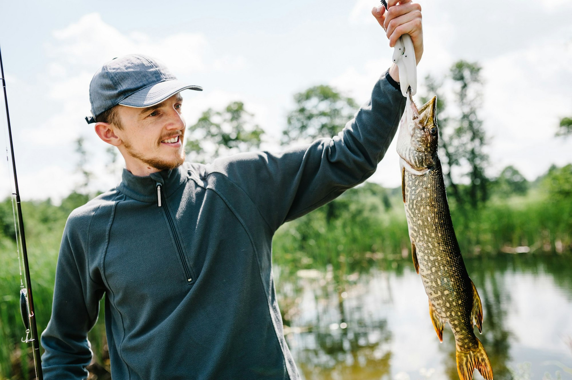 Happy cheerful young fisherman hold a big fish pike on a background of lake and nature. Fishing