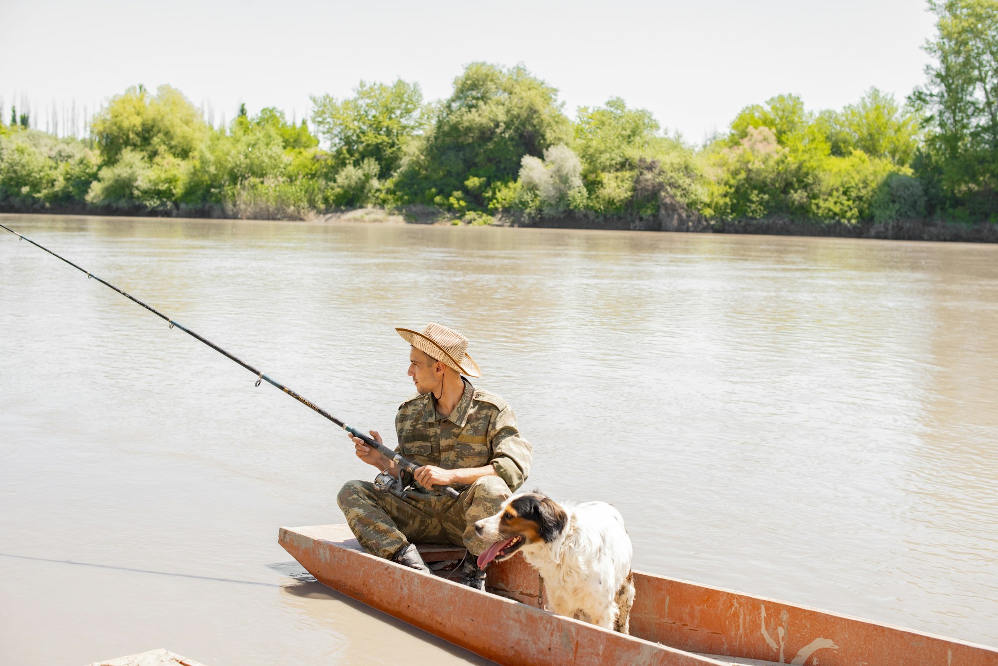 Relaxed, pensive male angler fishing from boat with dog in sunny day.